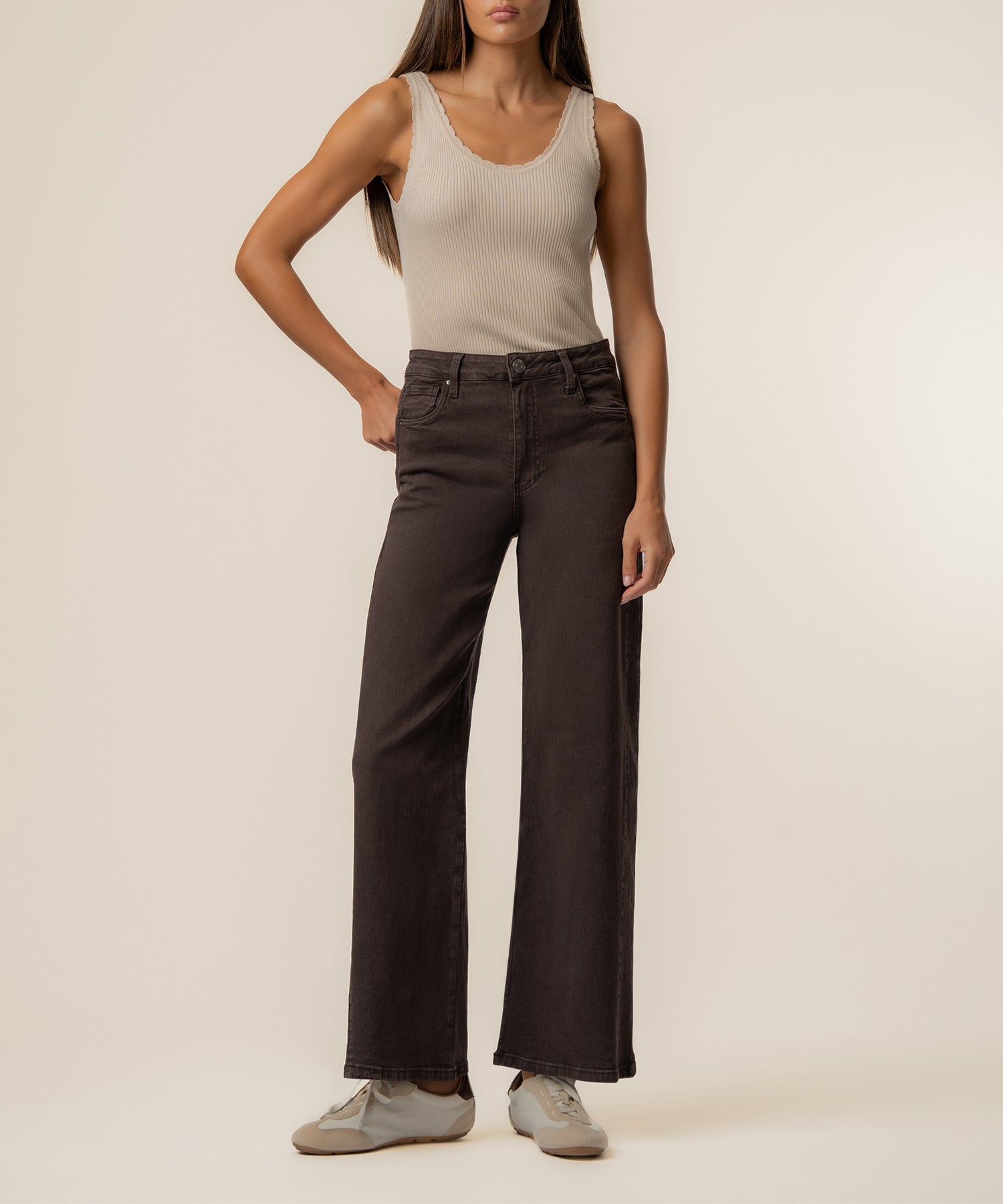 Woman wearing beige ribbed tank top and chocolate brown high-rise wide-leg jeans with white sneakers.
