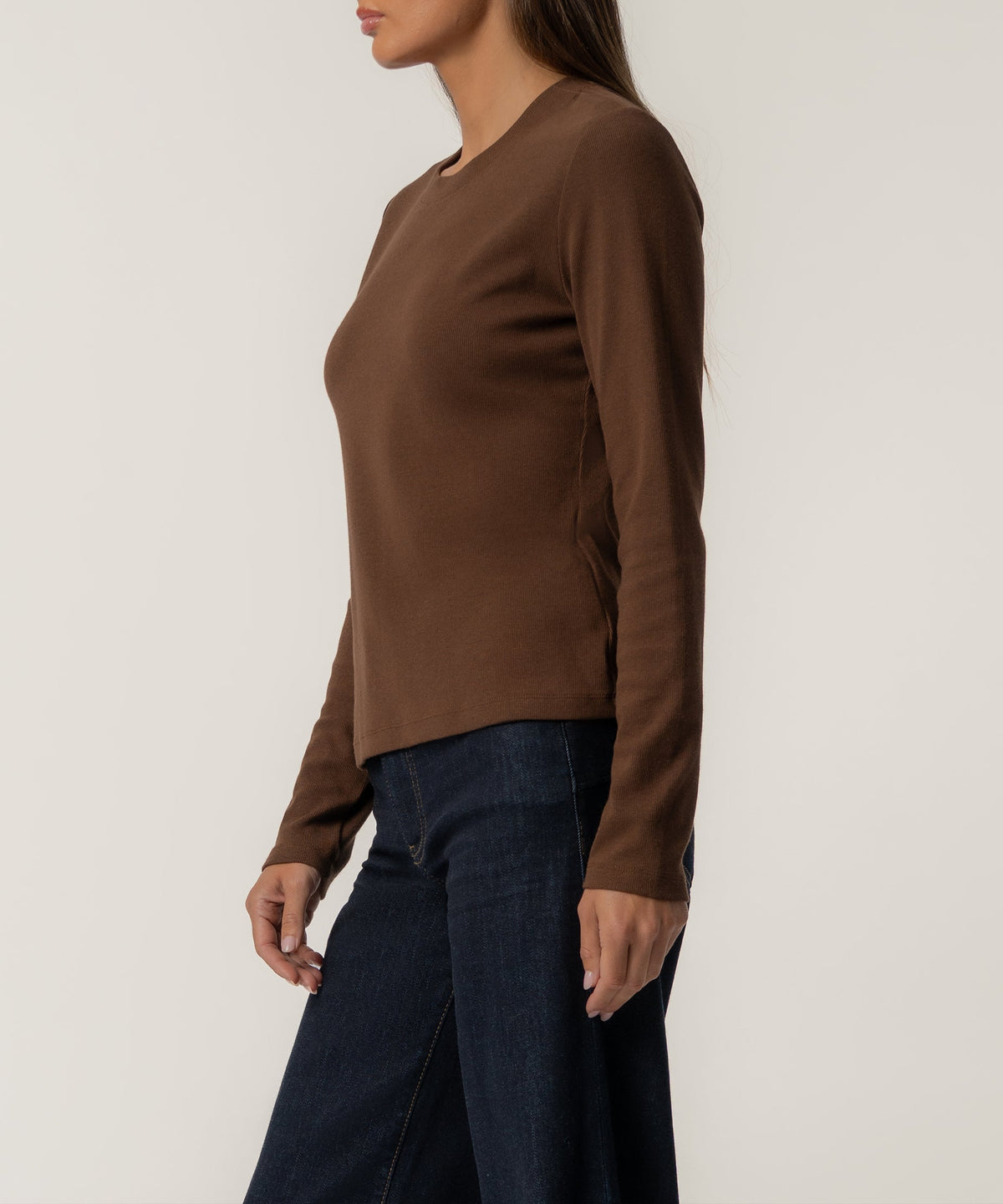Chocolate brown long-sleeve knit top with crew neckline on model wearing dark denim jeans.