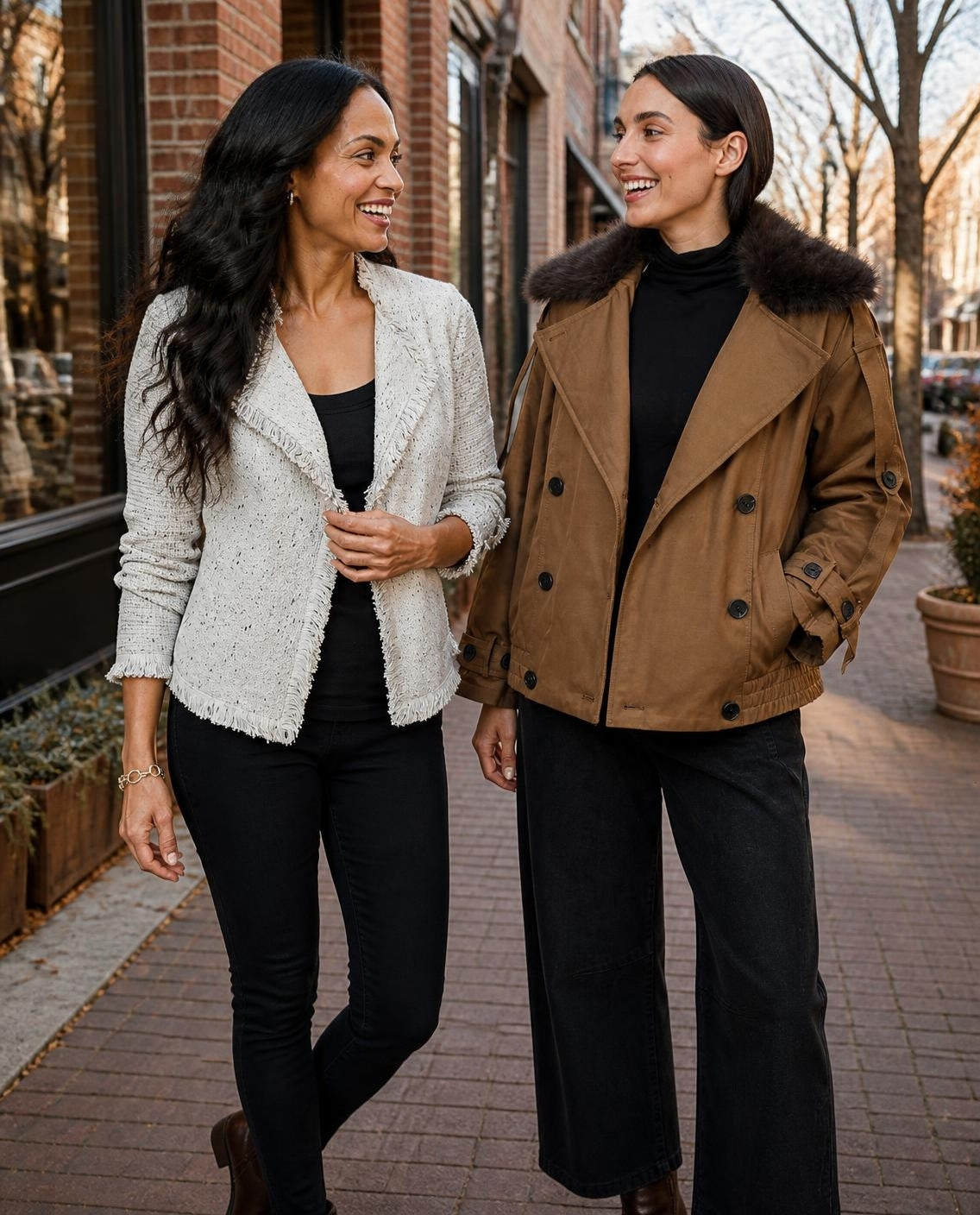 Two women in a fringe knit jacket and a fur collar trench outside a brick boutique