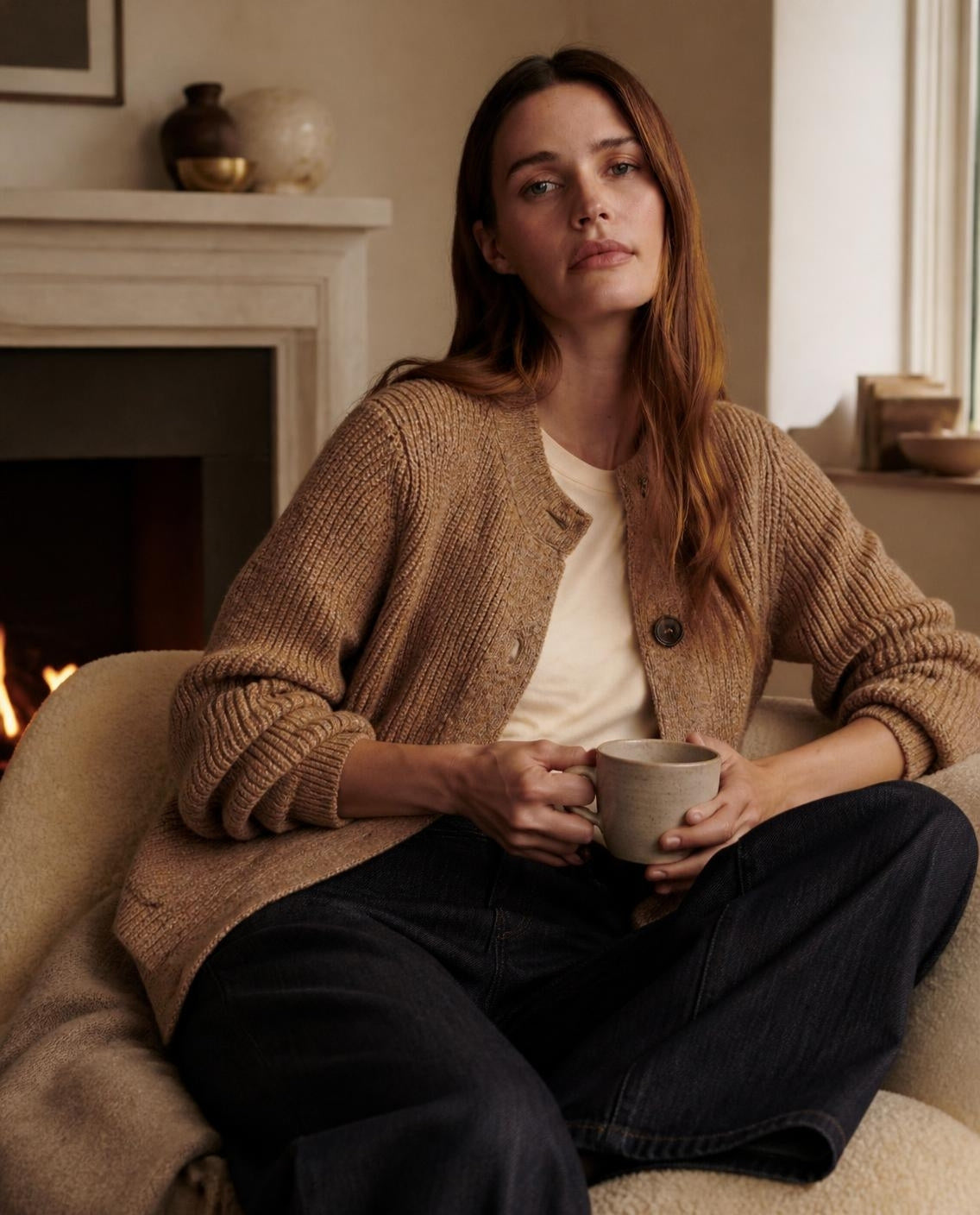 Woman in a golden bronze rib cardigan relaxing by a fireplace
