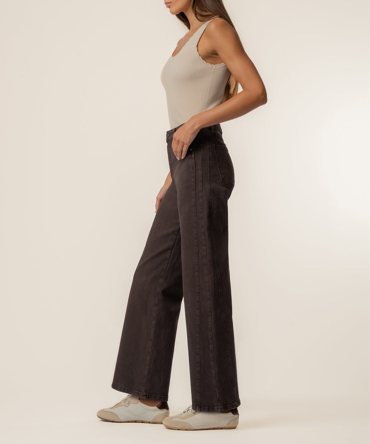 Woman wearing chocolate brown high-rise wide-leg jeans with a cream ribbed tank top and white sneakers.