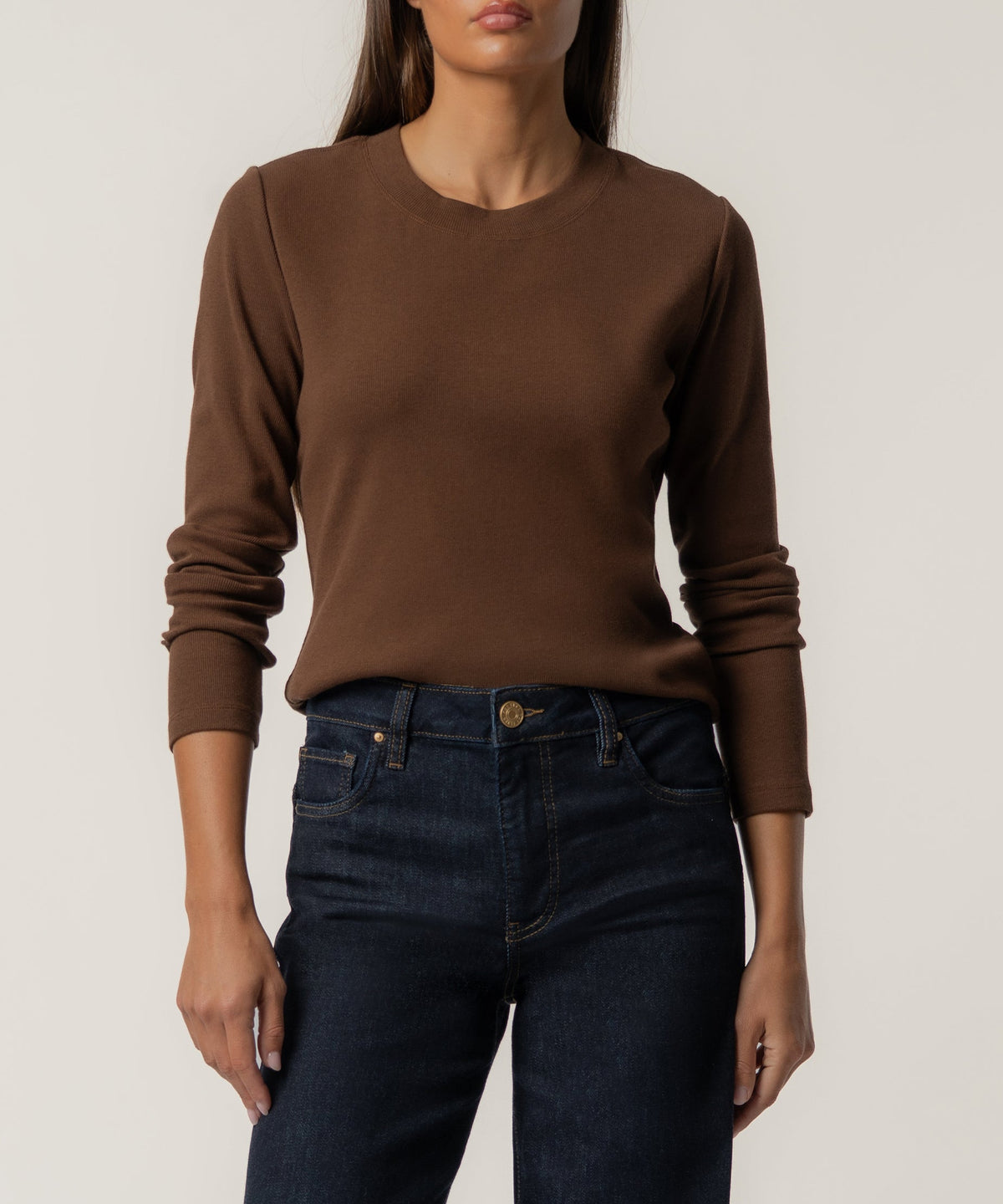 Brown long-sleeve crew neck knit top worn with dark denim jeans.