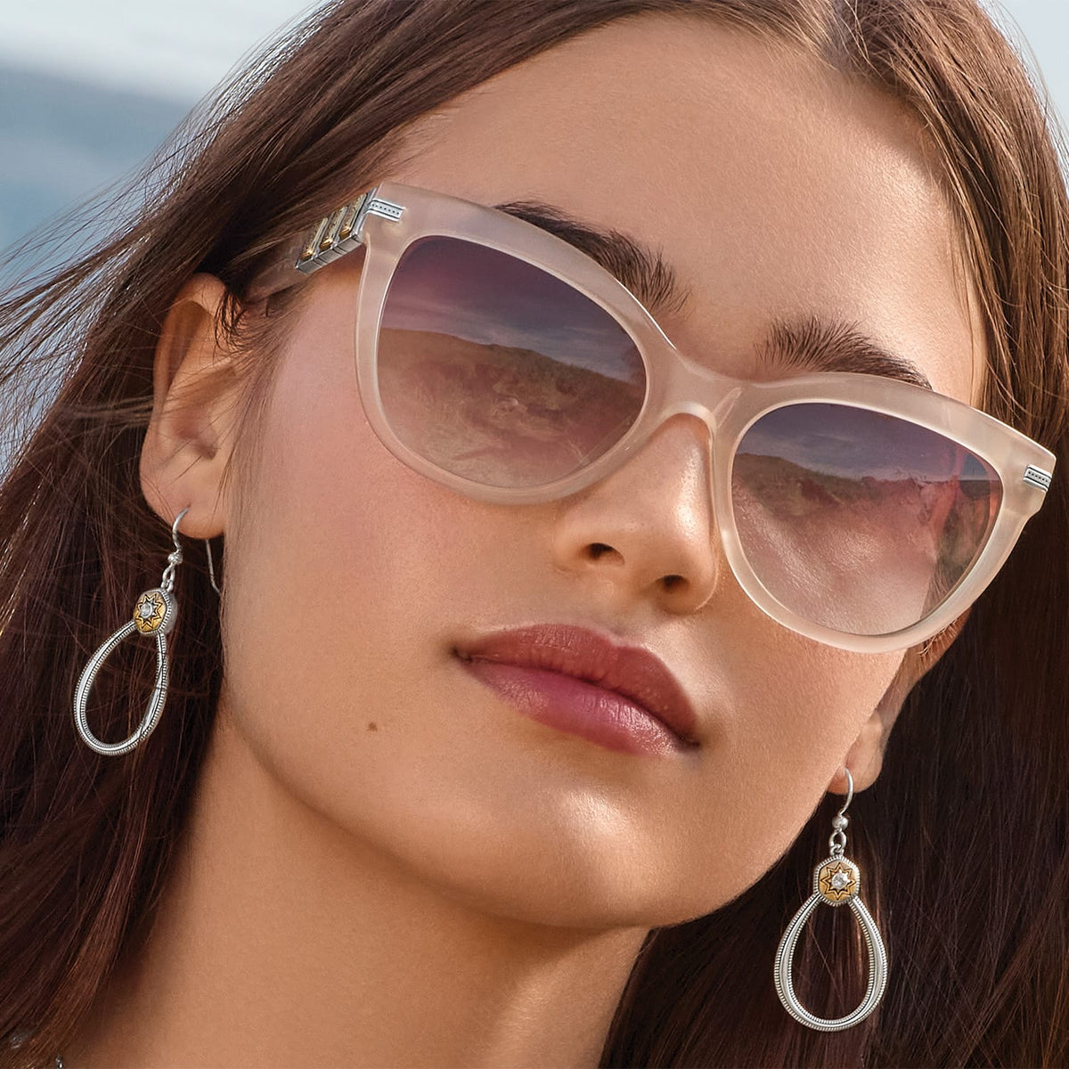 Model wearing Brighton silver teardrop earrings with two-tone star medallion and crystal accents, styled with sunglasses